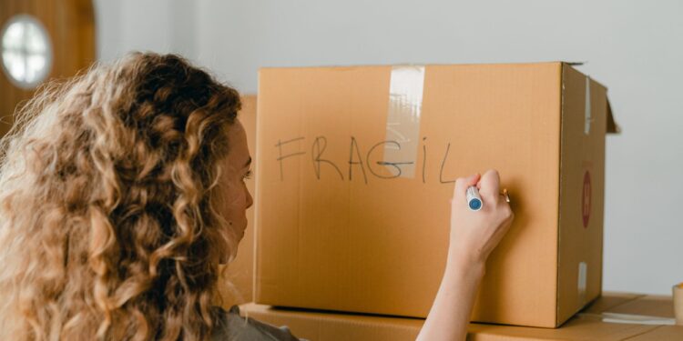 A girl writing the word 'Fragile' on a cardboard box