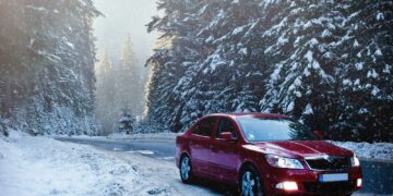 A red sedan in the middle of a snowy forest road