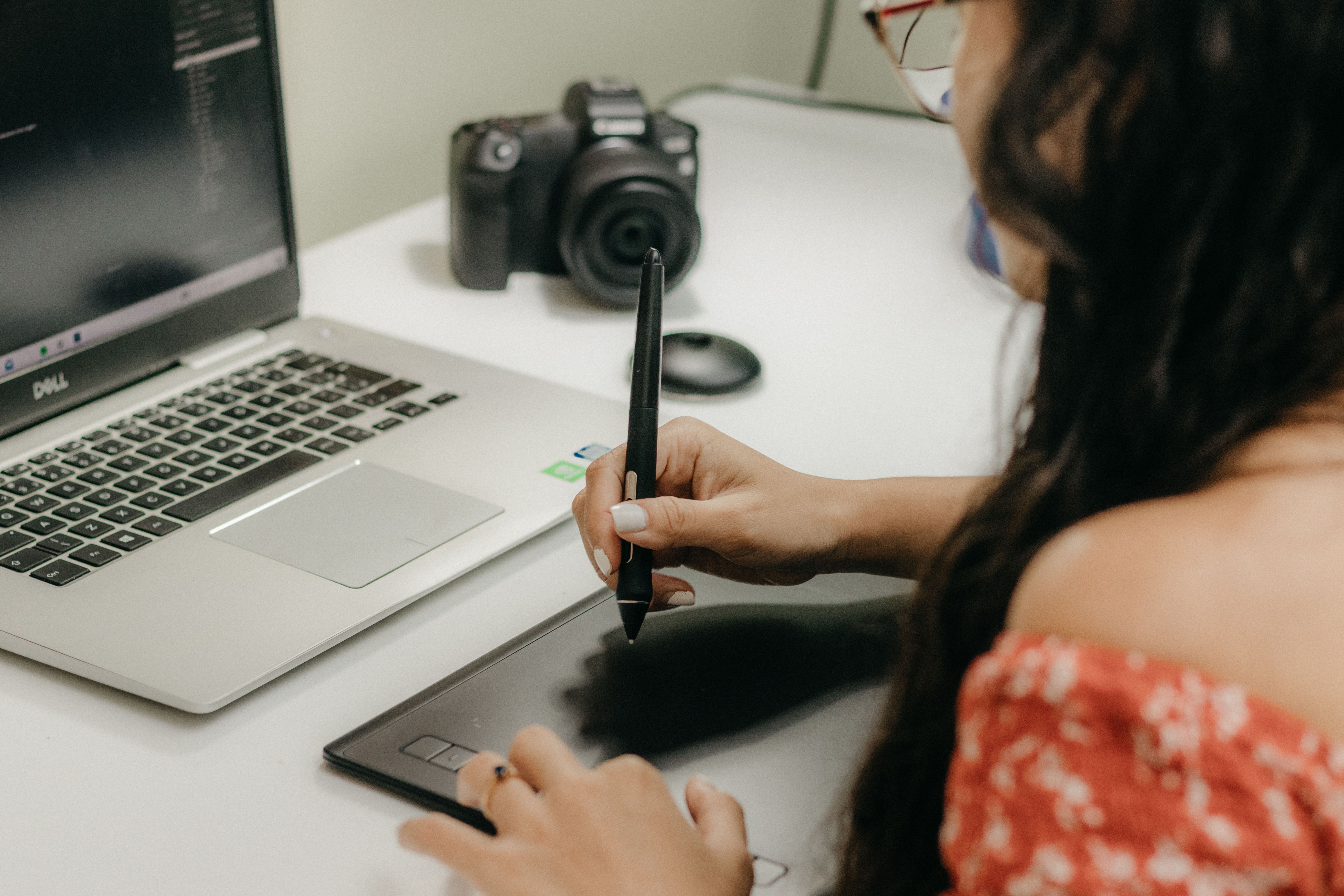 Designer using a tablet and stylus beside a laptop, representing creation and resizing of digital ad graphics.